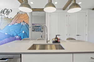 Kitchen featuring a center island, white cabinetry, beam ceiling, sink, and dishwasher