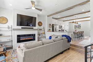 Living room with light hardwood / wood-style floors, ceiling fan, beamed ceiling, and a large fireplace