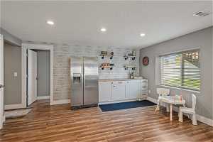 Kitchen with wood-type flooring, natural light, stainless steel refrigerator, and white cabinetry