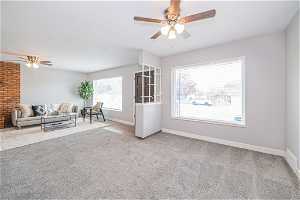 Unfurnished living room featuring a healthy amount of sunlight, ceiling fan, carpet, and brick wall