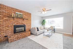 Carpeted living room featuring a fireplace, ceiling fan, and brick wall