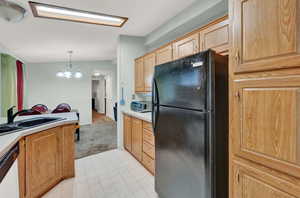 Kitchen featuring a notable chandelier, dishwasher, light tile flooring, black fridge, and decorative light fixtures