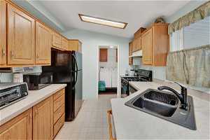 Kitchen with gas range oven, washing machine and clothes dryer, sink, light tile floors, and lofted ceiling