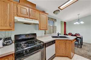 Kitchen with black gas range oven, sink, dishwasher, light colored carpet, and an inviting chandelier