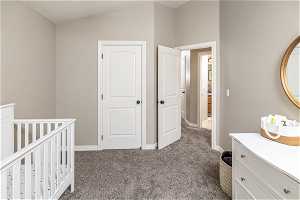 Unfurnished bedroom featuring a closet, a nursery area, dark carpet, and vaulted ceiling