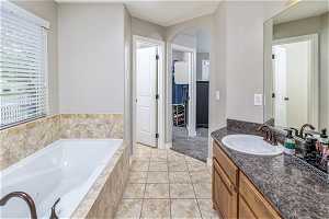 Bathroom with tile flooring, a relaxing tiled bath, vanity with extensive cabinet space, and a wealth of natural light