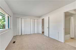 Unfurnished bedroom featuring light colored carpet, ensuite bathroom, and multiple closets