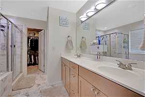 Bathroom featuring walk in shower, tile flooring, vanity with extensive cabinet space, and dual sinks