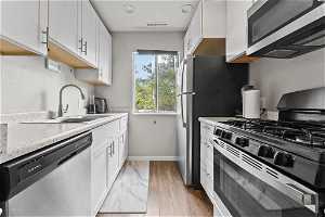 Kitchen with sink, light wood-type flooring, stainless steel appliances, and white cabinetry