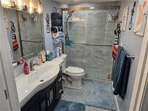 Bathroom with a shower with shower door, toilet, oversized vanity, and tile floors