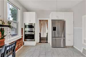 Kitchen with stainless steel appliances, white cabinets, and light tile flooring