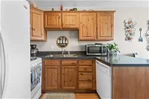 Kitchen with sink, white appliances, kitchen peninsula, and light hardwood / wood-style flooring