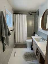 Bathroom featuring tile walls, toilet, tile flooring, and vanity