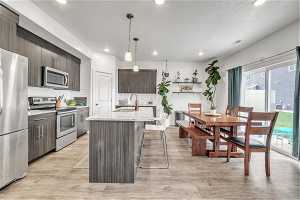 Kitchen with backsplash, appliances with stainless steel finishes, light hardwood / wood-style flooring, and a center island with sink