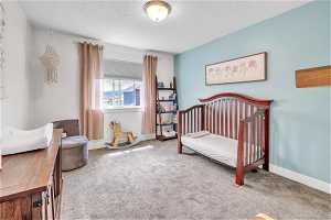 Carpeted bedroom featuring a nursery area and a textured ceiling