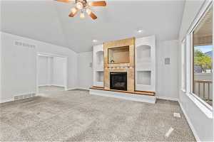 Unfurnished living room with built in shelves, carpet, vaulted ceiling, and a fireplace