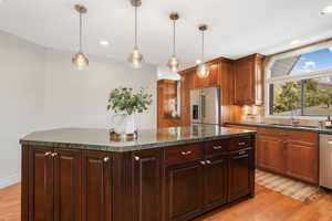 Kitchen featuring a kitchen island, light hardwood floors, backsplash, decorative light fixtures, and stainless steel appliances