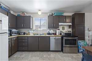 Kitchen featuring appliances with stainless steel finishes, dark brown cabinets, sink, and light tile flooring