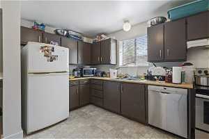 Kitchen with sink, appliances with stainless steel finishes, extractor fan, dark brown cabinetry, and light tile floors
