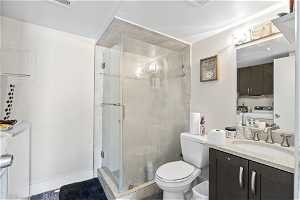 Bathroom with a shower with shower door, toilet, washer and dryer, vanity, and tile floors