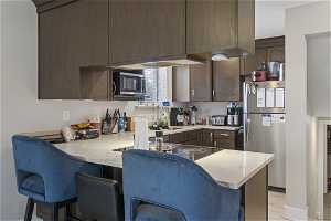 Kitchen with light stone counters, appliances with stainless steel finishes, a breakfast bar, sink, and kitchen peninsula