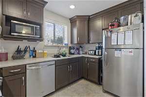 Kitchen featuring stainless steel appliances, dark brown cabinetry, sink, and light tile flooring