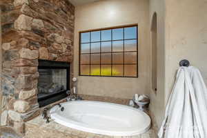 Primary bathroom featuring a stone fireplace and a bath to relax in