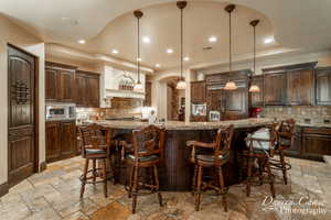 Kitchen with hanging light fixtures, stainless steel appliances, backsplash, and light tile floors