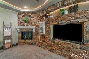 Living room with carpet flooring, a stone fireplace, and a tray ceiling