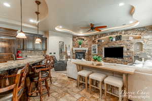 Living room featuring a fireplace, a raised ceiling, ceiling fan, and light tile floors