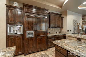 Kitchen featuring tasteful backsplash, dark brown cabinets, light tile floors, and light stone counters