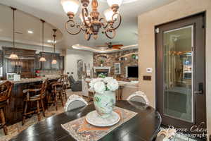 Tiled dining space featuring ceiling fan with notable chandelier and a stone fireplace