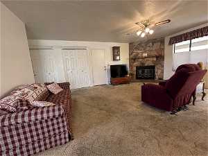 Living room featuring a textured ceiling, carpet floors, ceiling fan, and a stone fireplace