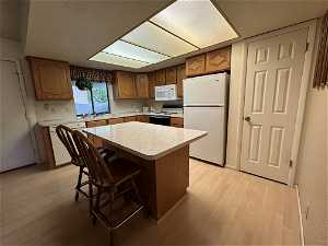 Kitchen with a kitchen island, light hardwood / wood-style flooring, white appliances, a breakfast bar area, and sink