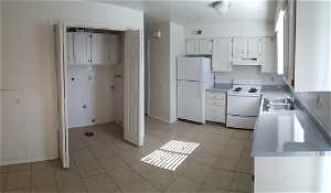 Kitchen with white cabinets, sink, white appliances, and light tile floors