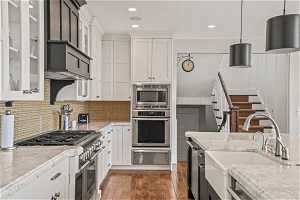 Kitchen featuring stainless steel appliances, decorative light fixtures, white cabinetry, backsplash, and light stone counters