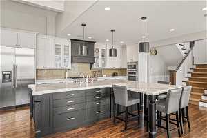 Kitchen with white cabinets, a center island with sink, stainless steel appliances, and dark hardwood / wood-style flooring