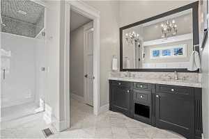 Bathroom with double sink vanity, a notable chandelier, tiled shower, and tile floors