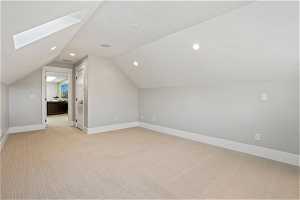 Additional living space with vaulted ceiling with skylight and light colored carpet