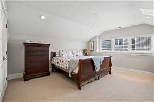 Bedroom with vaulted ceiling with skylight and light colored carpet