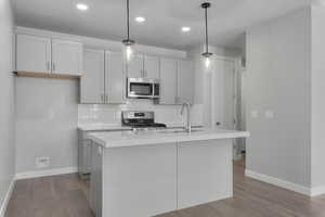 Kitchen featuring pendant lighting, an island with sink, sink, light hardwood / wood-style floors, and appliances with stainless steel finishes