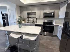 Kitchen with hardwood / wood-style floors, appliances with stainless steel finishes, backsplash, and gray cabinetry