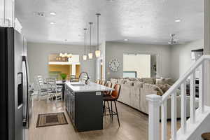 Kitchen with decorative light fixtures, stainless steel refrigerator with ice dispenser, light hardwood / wood-style flooring, white cabinetry, and sink