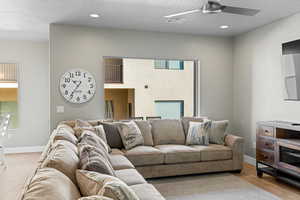 Living room featuring a textured ceiling, ceiling fan, and light wood-type flooring