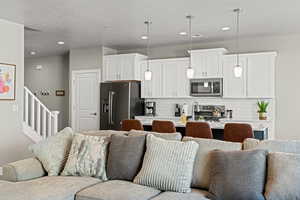 Kitchen featuring hanging light fixtures, white cabinets, stainless steel appliances, tasteful backsplash, and an island with sink