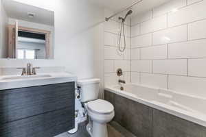 Full bathroom with tiled shower / bath, toilet, oversized vanity, and tile flooring