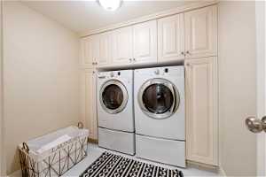 Washroom with cabinets, light tile floors, and washer and clothes dryer