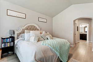 Bedroom with light hardwood / wood-style flooring, vaulted ceiling, and ensuite bathroom