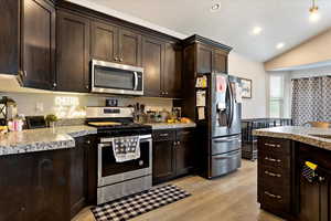 Kitchen featuring appliances with stainless steel finishes, dark brown cabinetry, vaulted ceiling, and light hardwood / wood-style floors