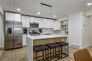 Kitchen featuring appliances with stainless steel finishes, hanging light fixtures, light hardwood / wood-style floors, tasteful backsplash, and white cabinetry